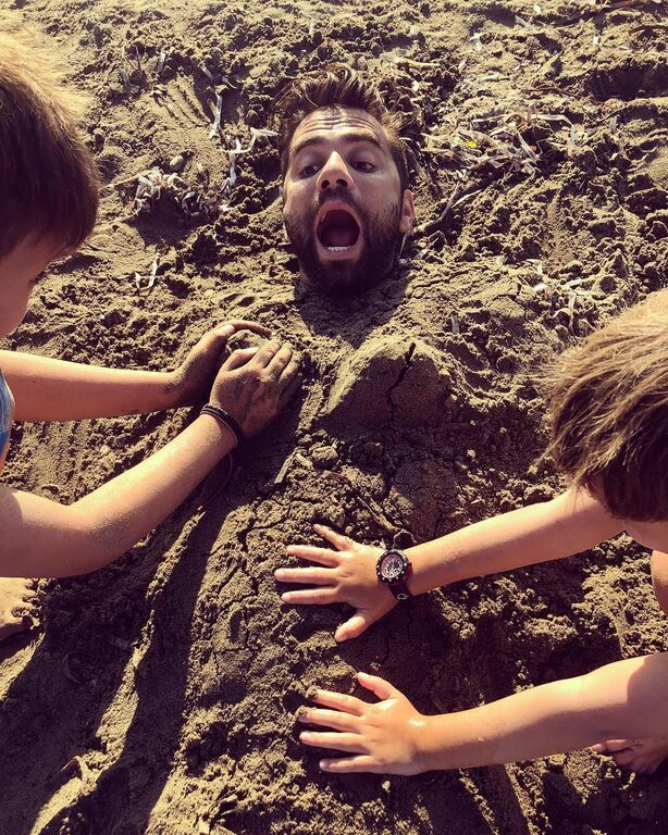 Ο Θοδωρής Μαραντίνης ποζάρει κάνοντας μία αστεία γκριμάτσα, ενώ είναι θαμμένος κάτω από την άμμο.