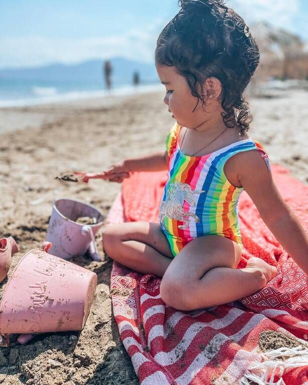 Η μικρή Μελίτα παίζει στην παραλία με ένα τέλειο ολόσωμο rainbow μαγιό με Μονόκερό.