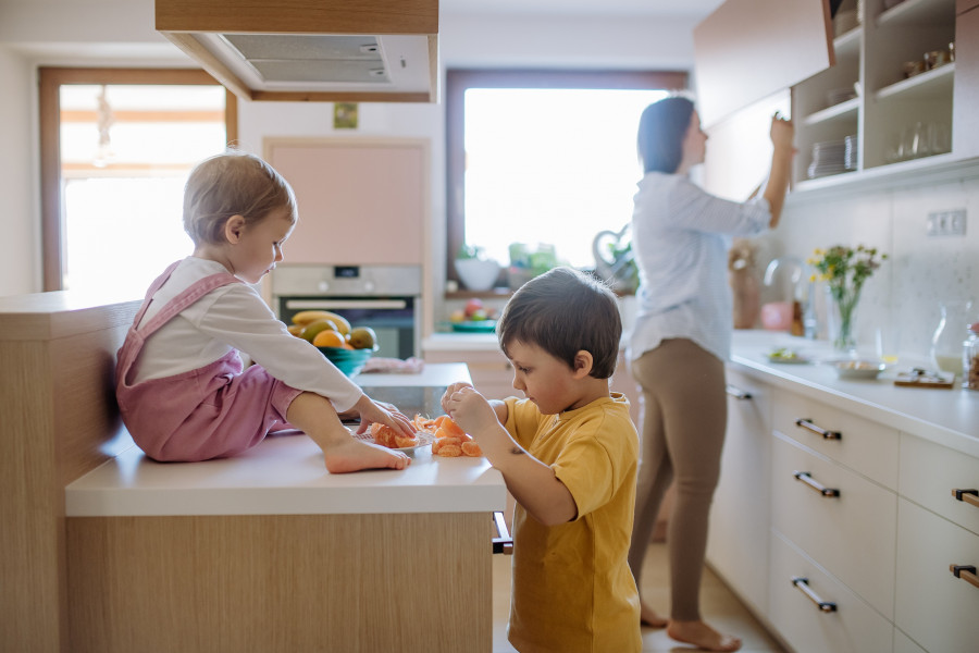 Mother Of Two Little Children Preparing Fruit Snack In Kitchen At Home.